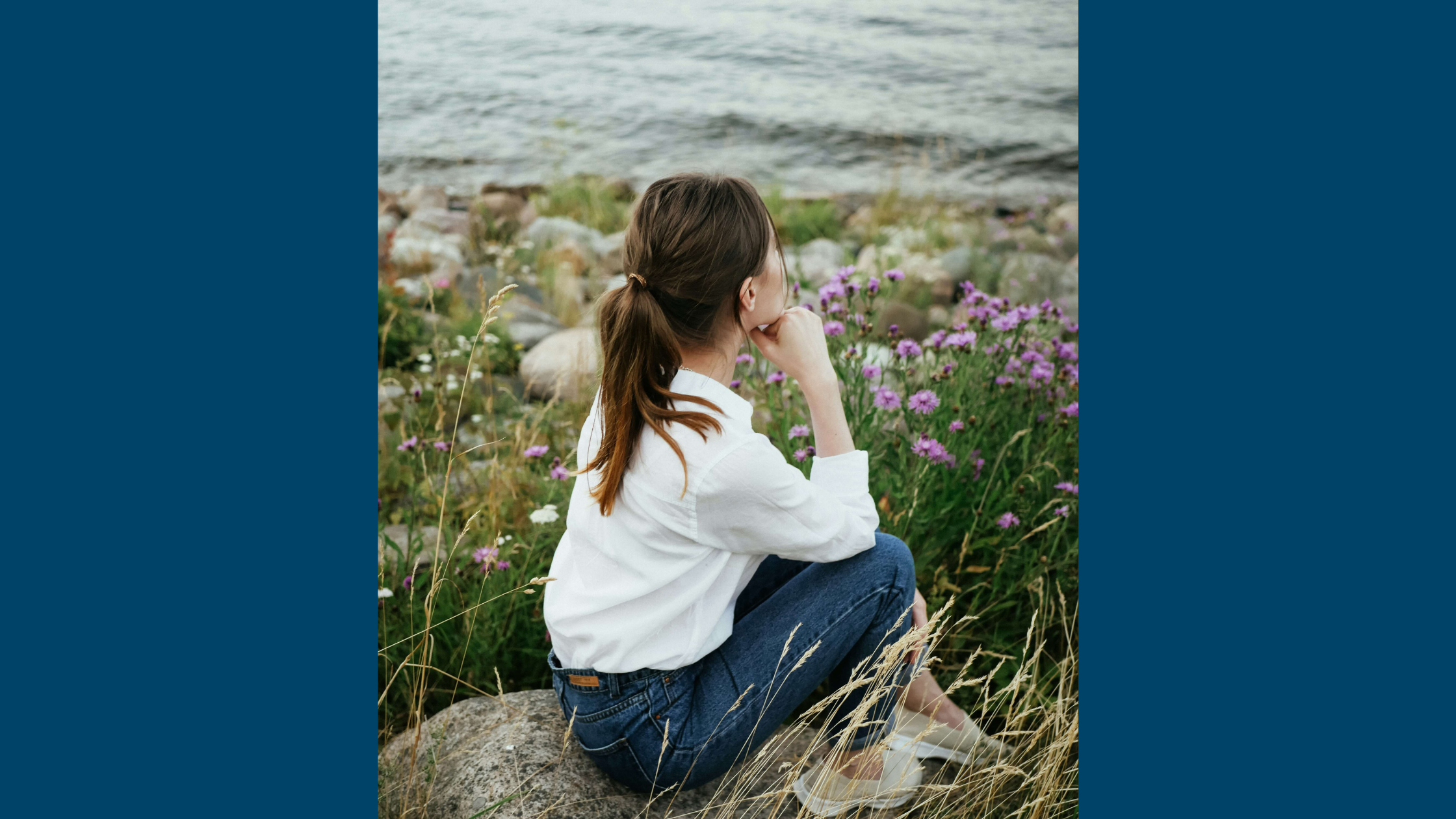 Woman sitting on rock overlooking water.